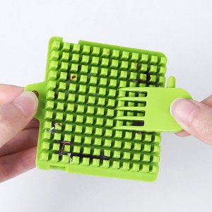 Green vegetable chopper grid with a cleaning tool being inserted, showing small food remnants.