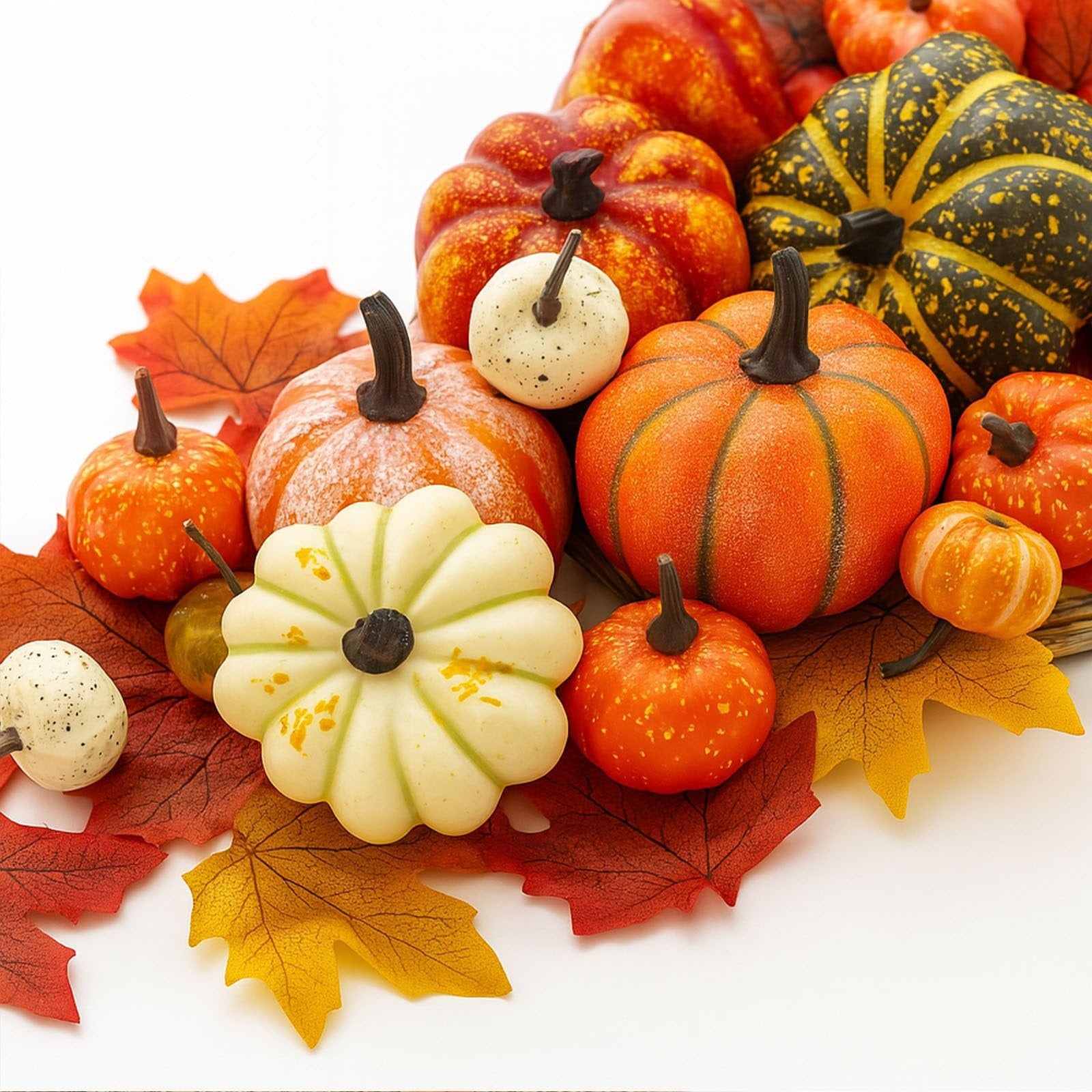 Assortment of artificial pumpkins and faux maple leaves in fall colors on a white background.