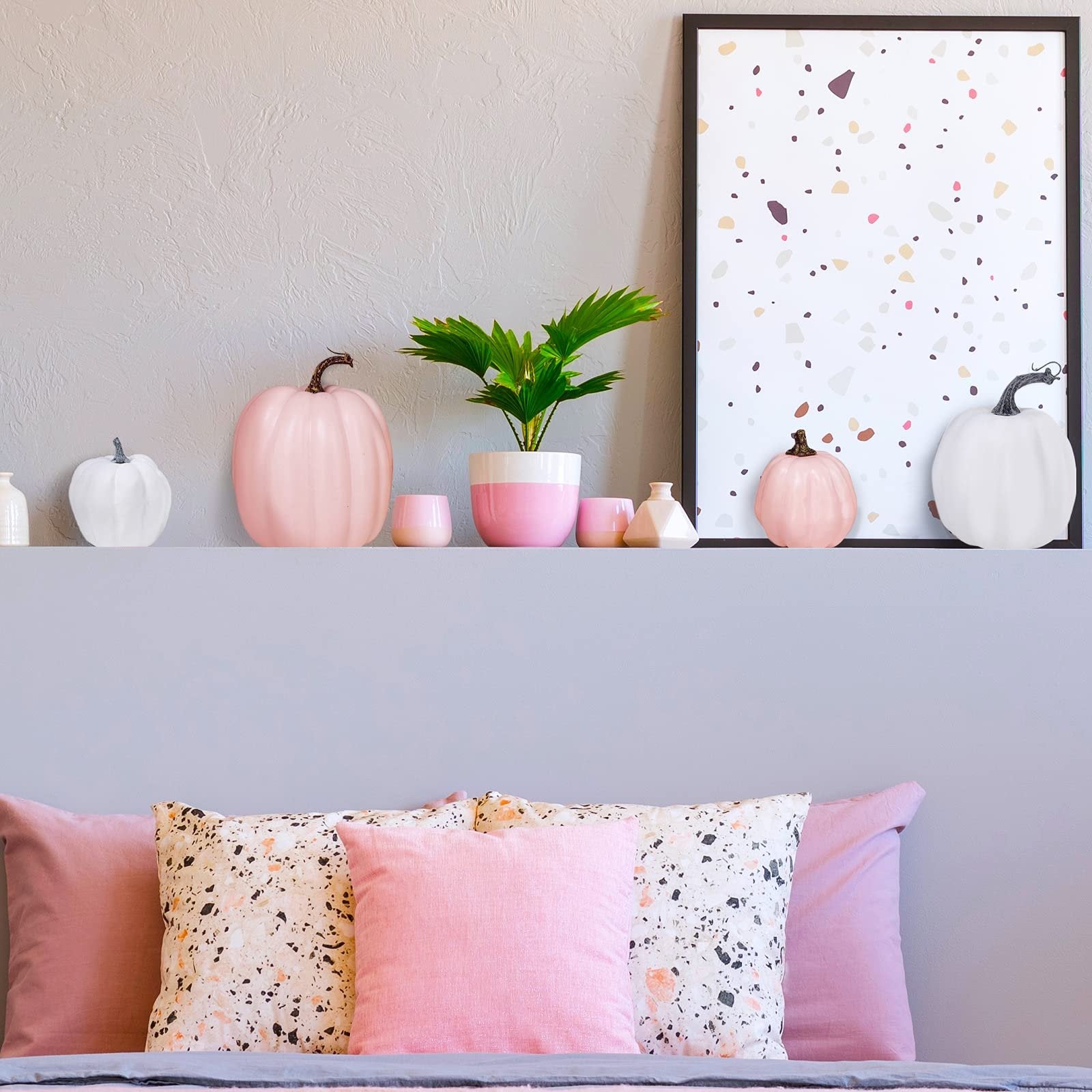 Assorted pink and white faux pumpkins and decorative vases on a shelf above a bed with pink pillows.