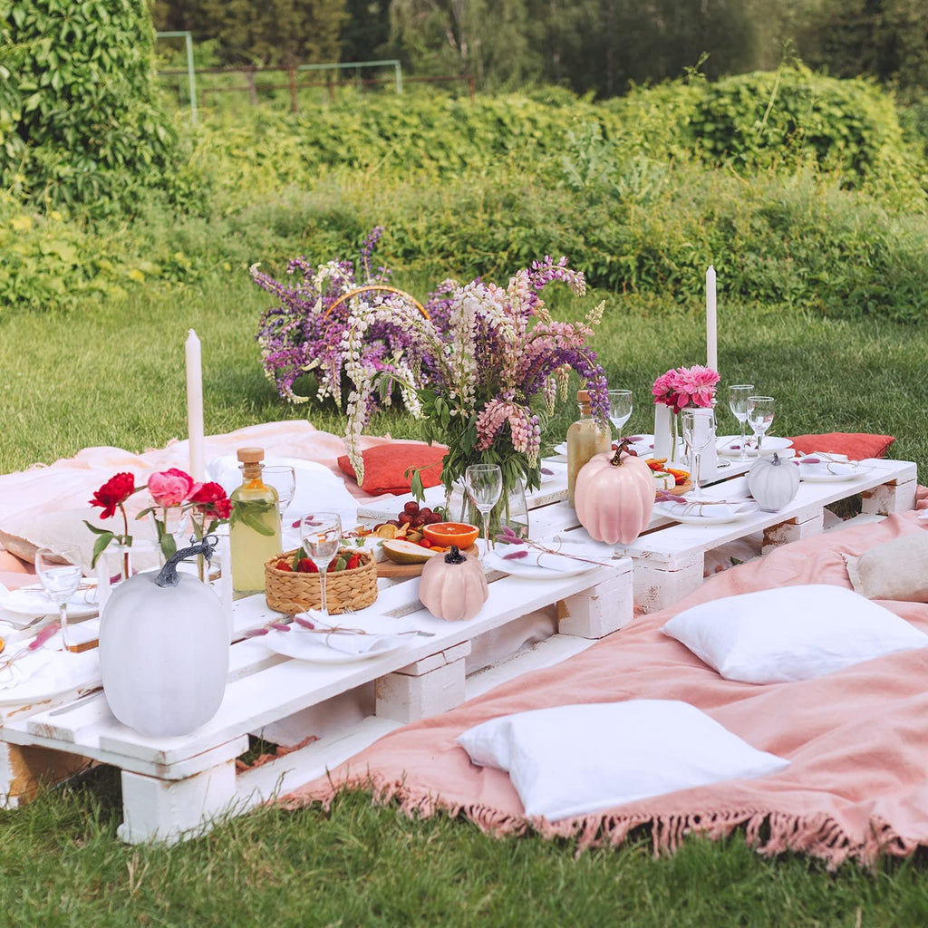 Assorted faux foam pumpkins arranged on a picnic table setting with flowers and food