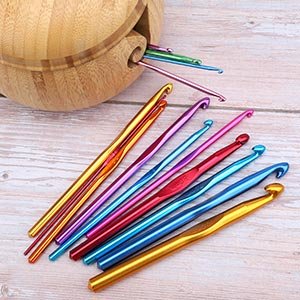 Multicolor aluminum crochet hooks of various sizes scattered on a wooden surface next to a bamboo storage container.