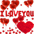 Red heart and letter balloons spelling I LOVE YOU with scattered red rose petals and a large heart made of petals