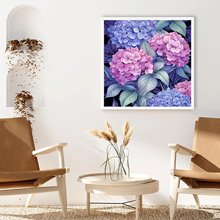 Framed 5D diamond painting of purple and pink hydrangeas hanging on a wall above a coffee table between two chairs.