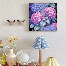 Framed diamond painting kit featuring purple and blue hydrangeas on a black background, displayed on a wall above a table with decor.