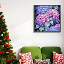 Framed diamond painting kit of pink and blue hydrangeas hanging on a wall above a green sofa with festive pillows, next to a decorated Christmas tree.