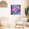 Living room scene with a framed diamond painting of pink and blue hydrangeas hanging on the wall above a chair.