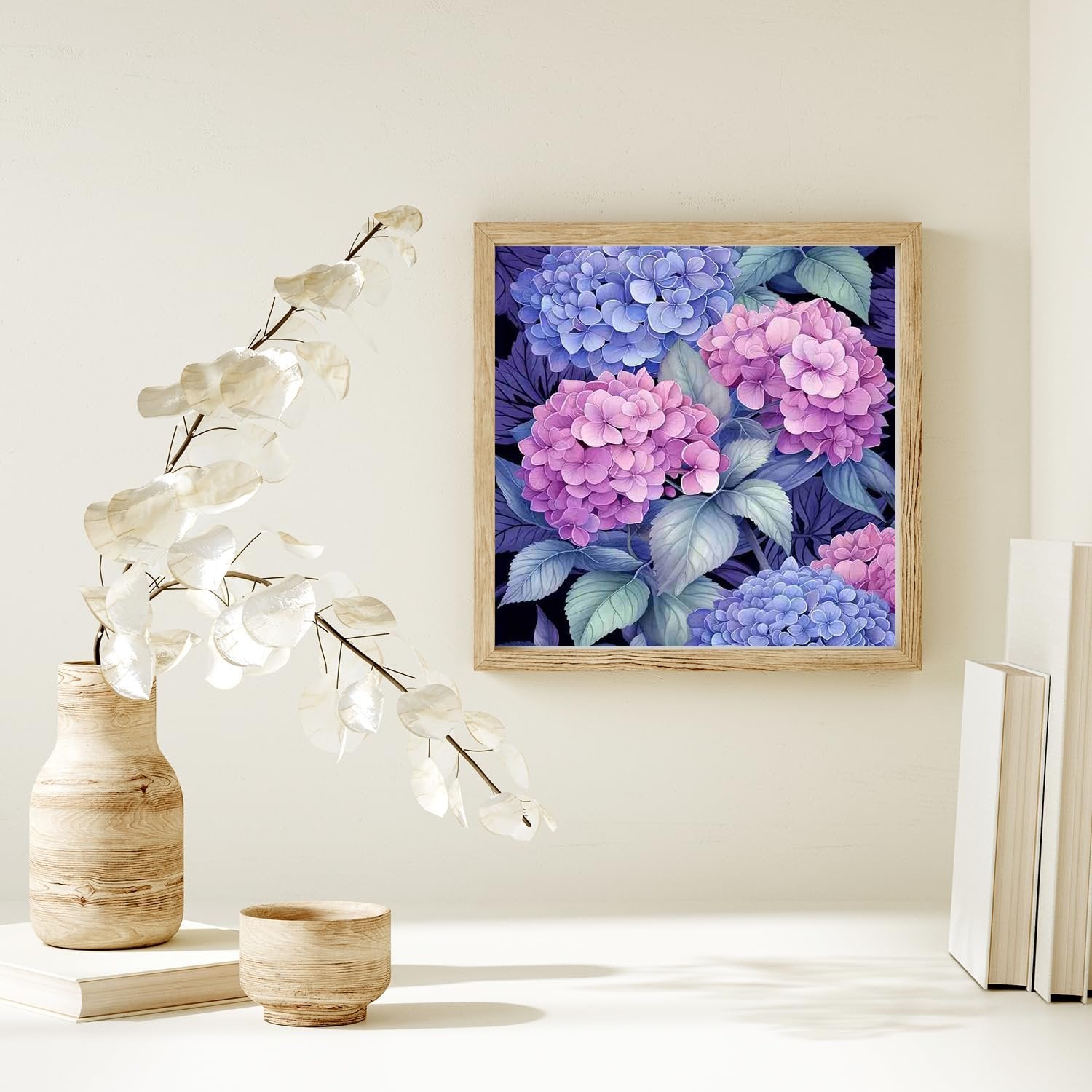 Framed diamond painting of pink and blue hydrangeas hanging on a wall above a vase and books.