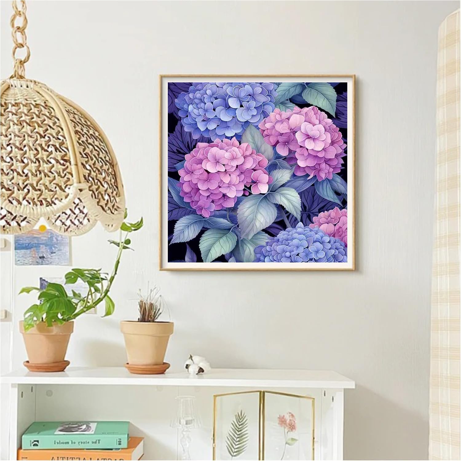 Framed diamond painting kit featuring pink and blue hydrangeas hanging on a wall above a shelf with plants and books.