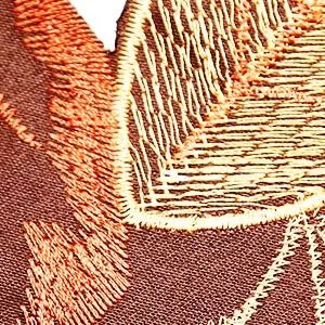 Close-up of embroidered fall leaves pattern on a fabric table runner, showing intricate stitching detail.