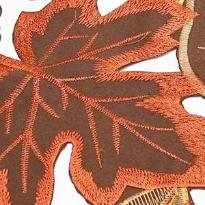 Close-up of a brown and orange embroidered fall leaf table runner, showing intricate stitching detail.