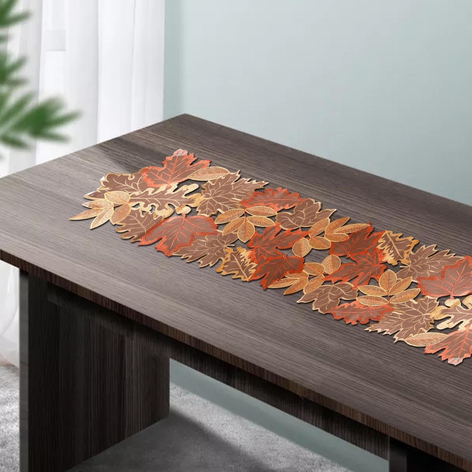 Embroidered fall leaves table runner on a dark wood table with sheer curtains in the background.