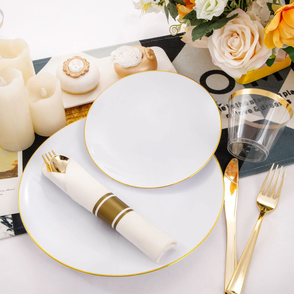 White disposable dinner plates with gold rims, gold cutlery, and a clear cup with gold rim, set on a table with candles and flowers.
