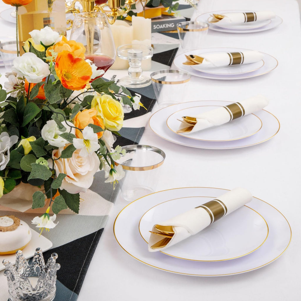 Table setting with white and gold rim disposable plates, cutlery, and cups, adorned with a floral arrangement.