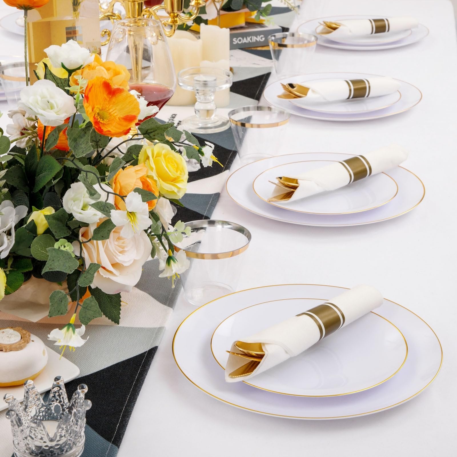 Table setting with white and gold rim disposable plates, cutlery, and cups, adorned with a floral arrangement.