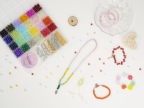 Bracelet making kit with assorted glass beads, findings, and finished jewelry pieces arranged on a white surface.