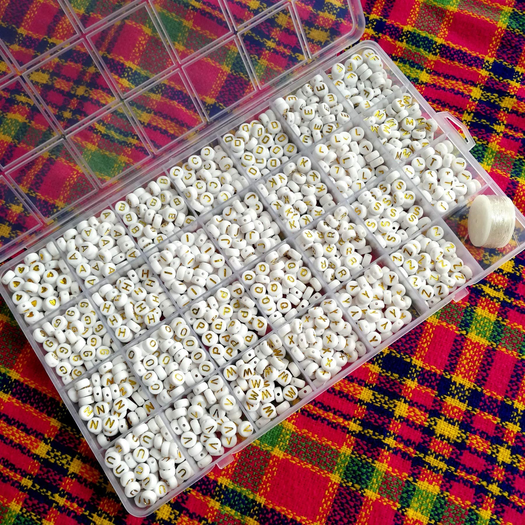 White acrylic alphabet beads with gold letters in a 28-compartment organizer box, with a roll of beading cord on the side.