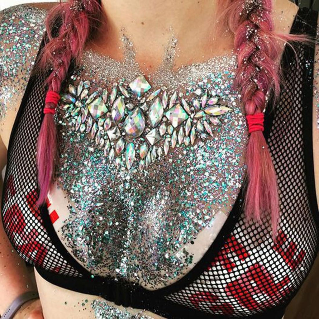 Woman with glitter and assorted acrylic gems applied to chest and face, wearing a black mesh top.