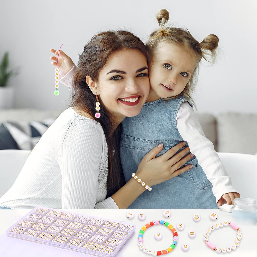 Woman and child smiling, holding jewelry made with letter beads. A tray of beads is in the foreground.