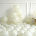 Pile of ivory white latex balloons in various sizes, some inflated and some deflated, against a white wall.