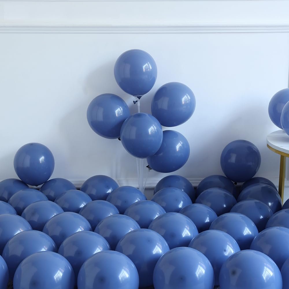 Dusty blue and ivory white balloons scattered on the floor and clustered on a stand against a white wall.