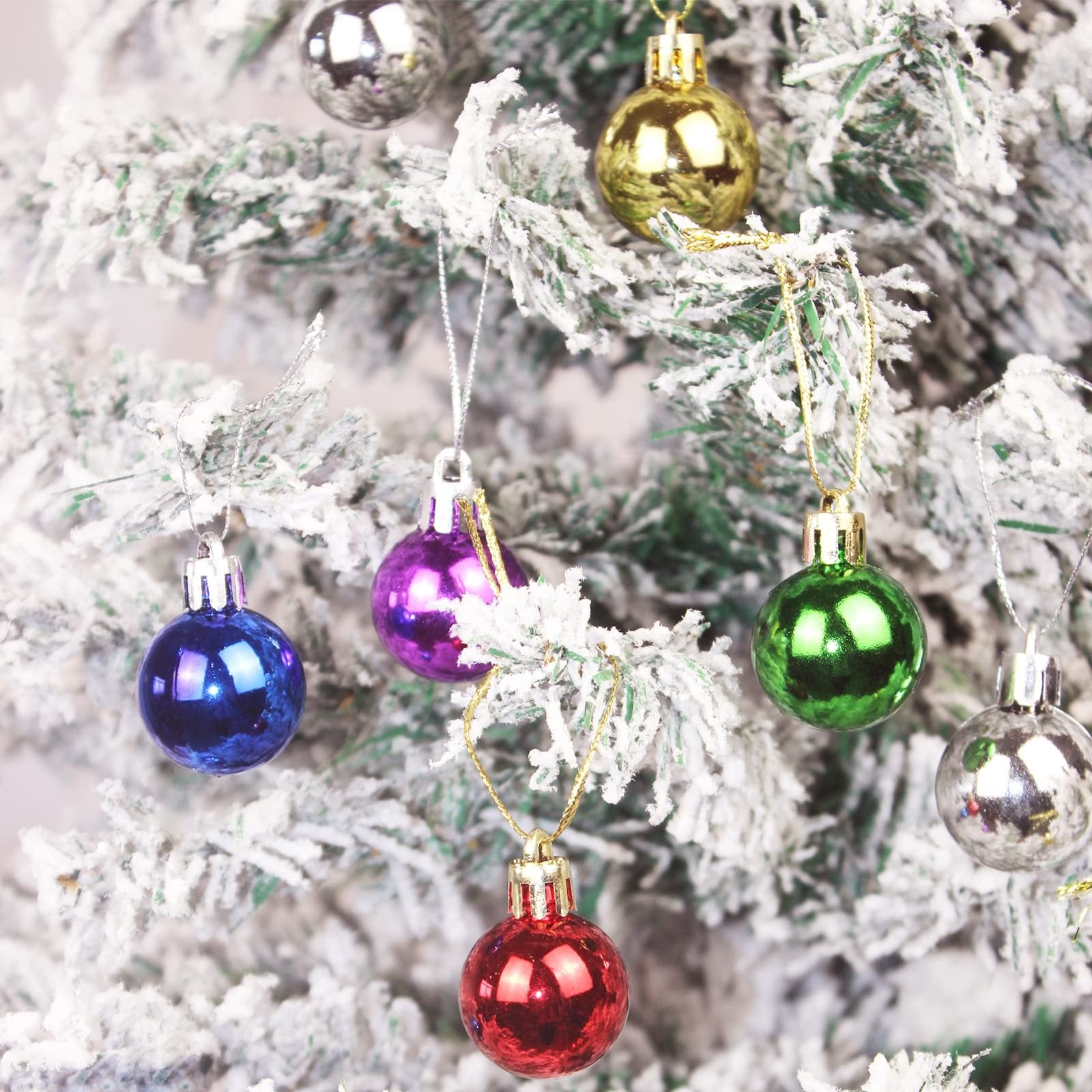 Assortment of small, colorful Christmas ball ornaments hanging on a flocked tree branch.
