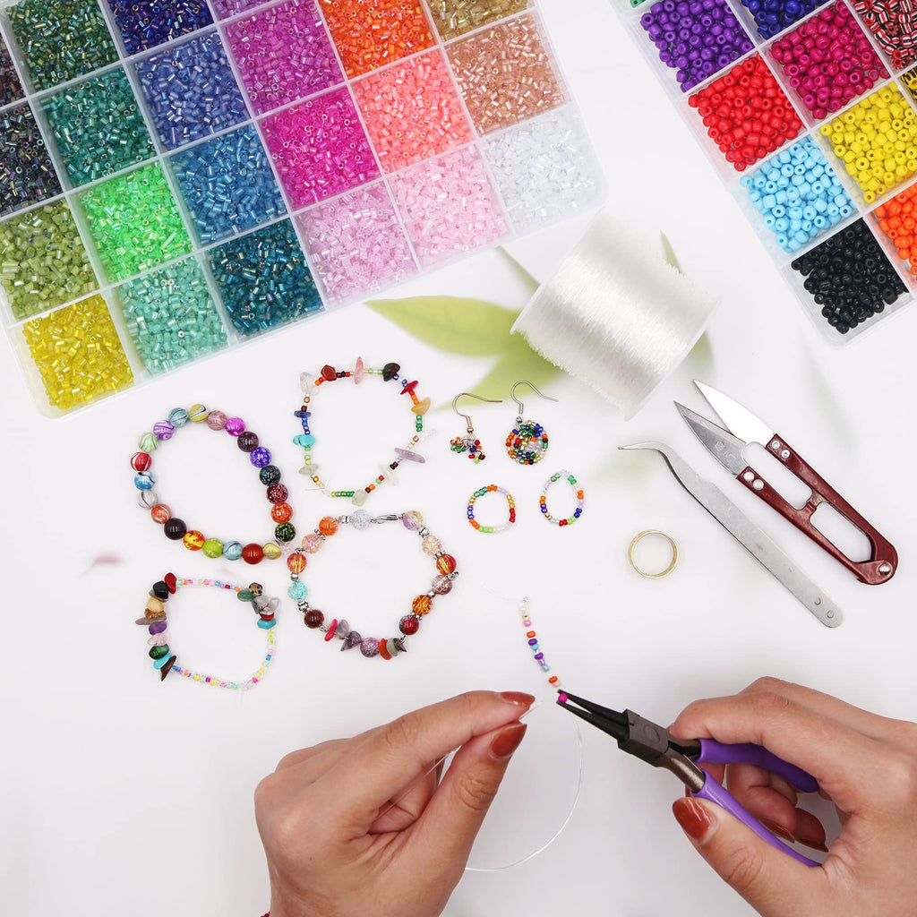 Hands using pliers to string colorful beads onto clear elastic cord, surrounded by bead containers, finished jewelry, and tools.