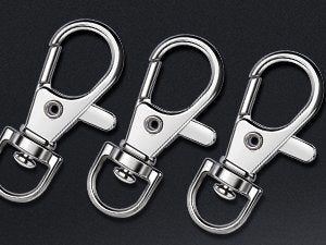 Three silver lobster claw clasps with D-rings, angled view on dark background.