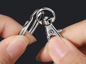 Close-up of hands assembling a keychain with a lobster clasp and jump ring.
