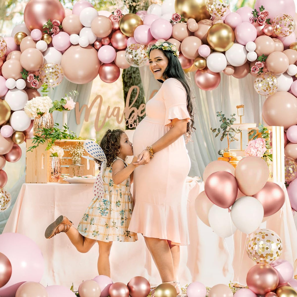 Pregnant woman and child at a baby shower with a large balloon arch and decorated table