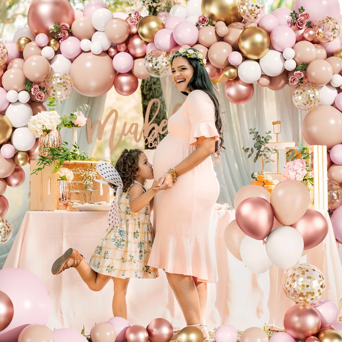 Pregnant woman and child at a baby shower with a large balloon arch and decorated table
