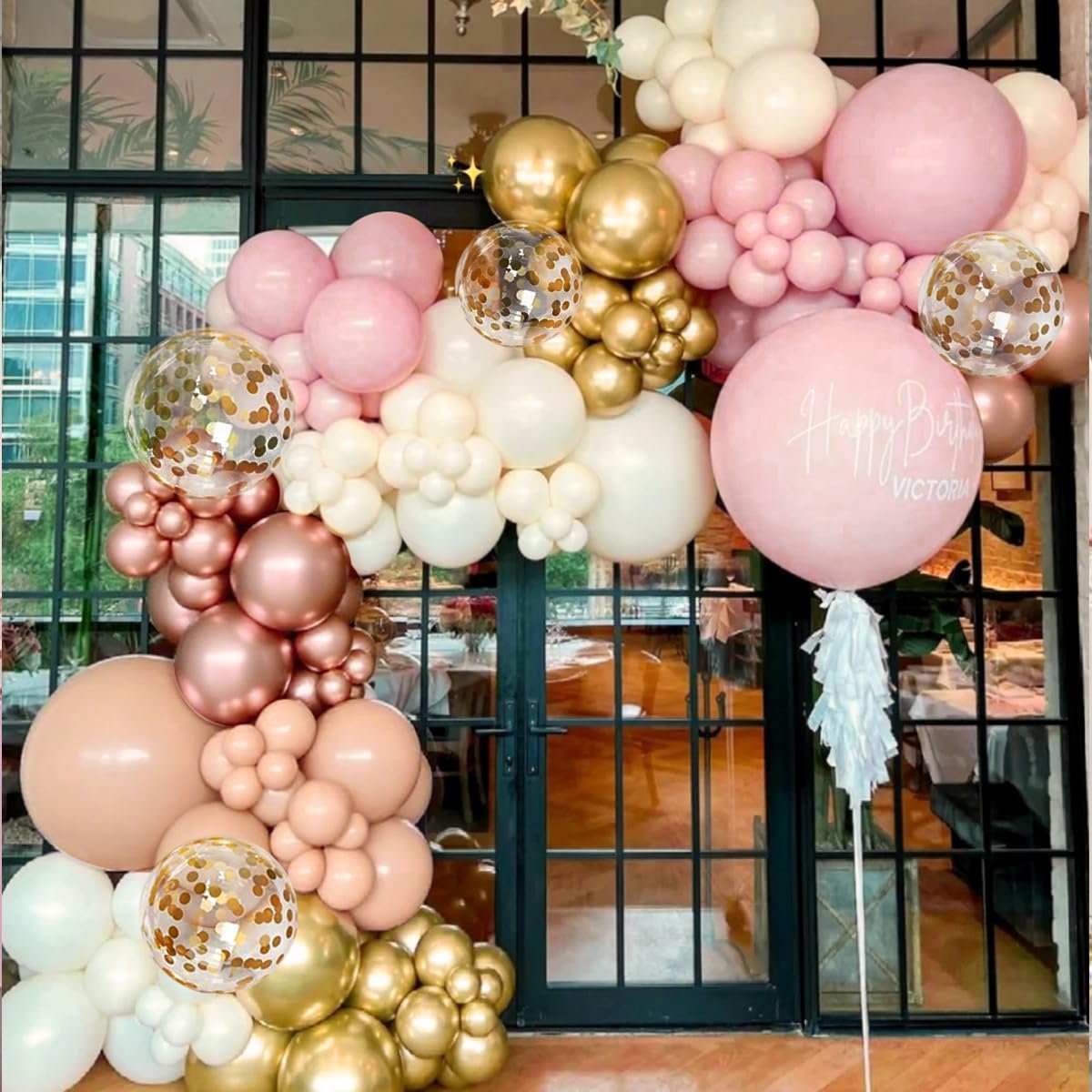 Balloon arch with rose gold, gold, white, nude, and pastel pink balloons, including confetti balloons and a large pink balloon with 'Happy Birthday Victoria' text.