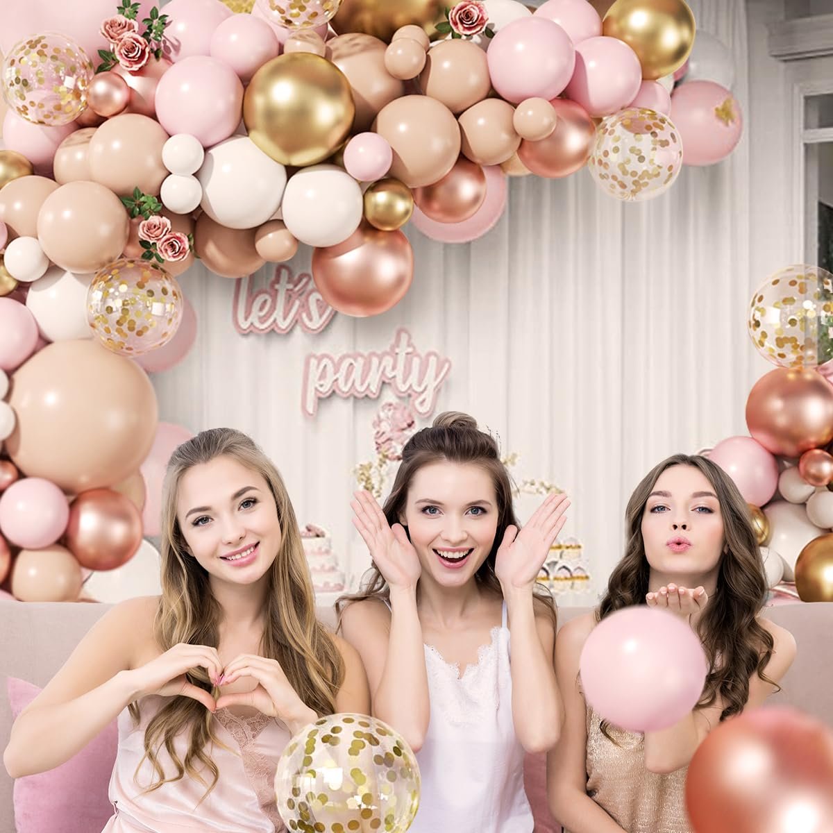 Three women posing with a rose gold balloon arch and confetti balloons for a party celebration.
