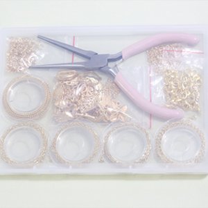 Jewelry making kit contents laid out in plastic compartments: copper chains, charm pendants, lobster clasps, jump rings, and pliers.