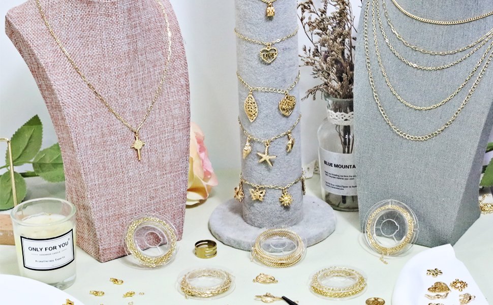 Gold jewelry making kit components displayed on a table, including necklaces on busts, chains on spools, and various charms.