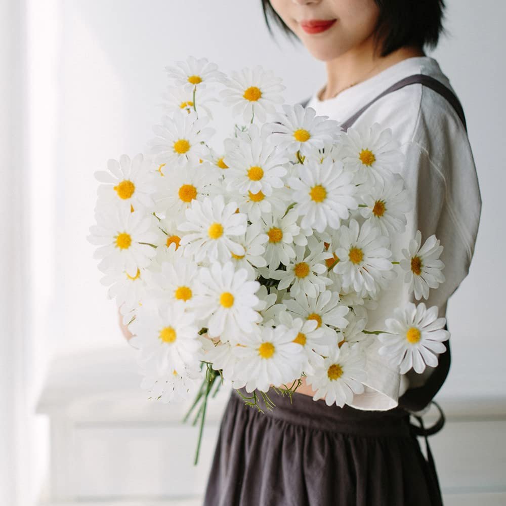 Woman holding a large bouquet of artificial white daisy flowers with yellow centers.