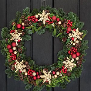Festive Christmas wreath with pinecones, red ornaments, and snowflakes hanging on a dark door.