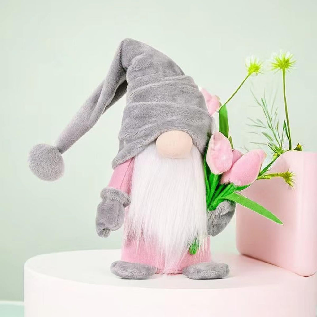 Plush gnome doll with a grey hat and pink outfit holding a bouquet of pink tulips, set against a light green background.
