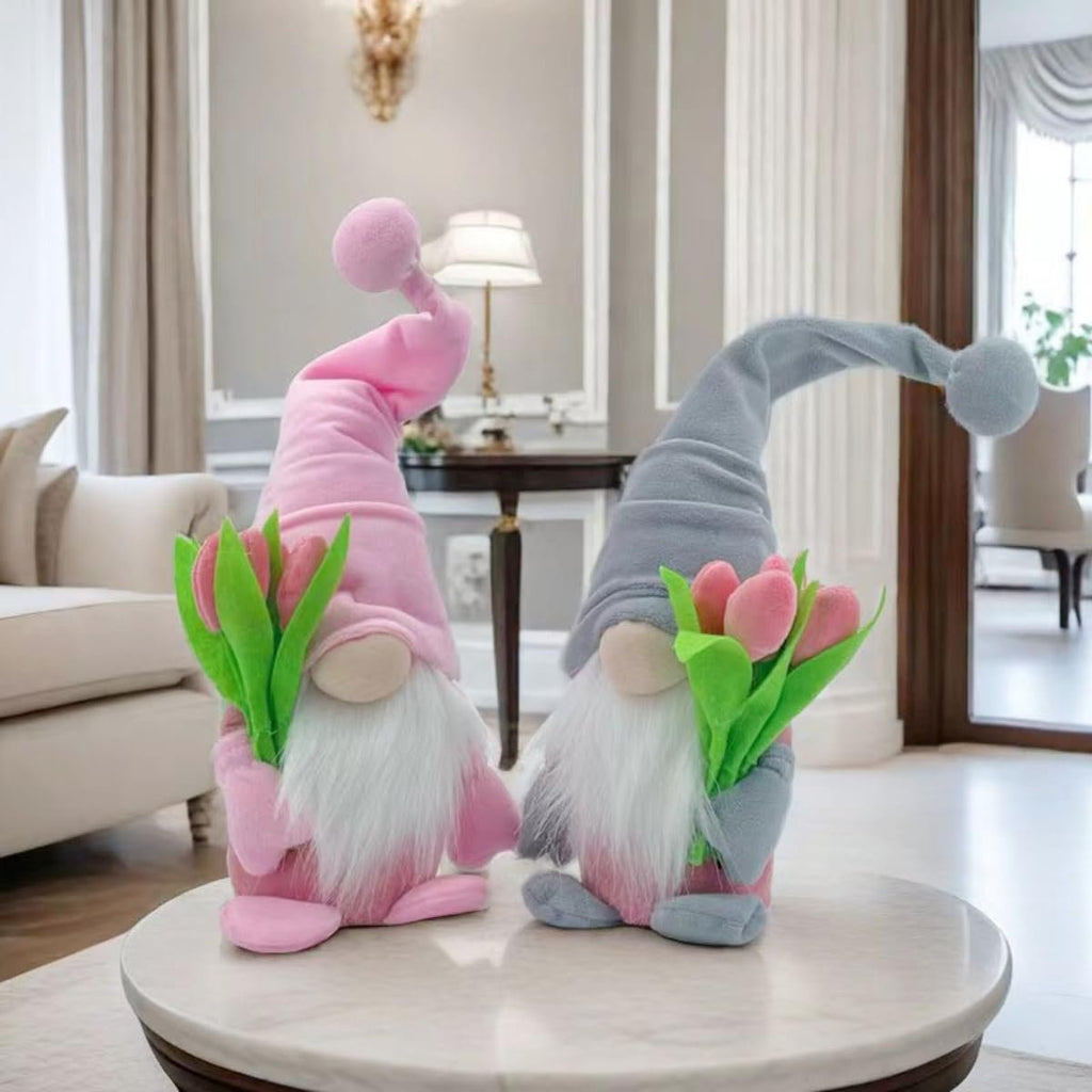 Two plush gnome dolls with tulips, one pink and one grey, sitting on a marble table in a living room.