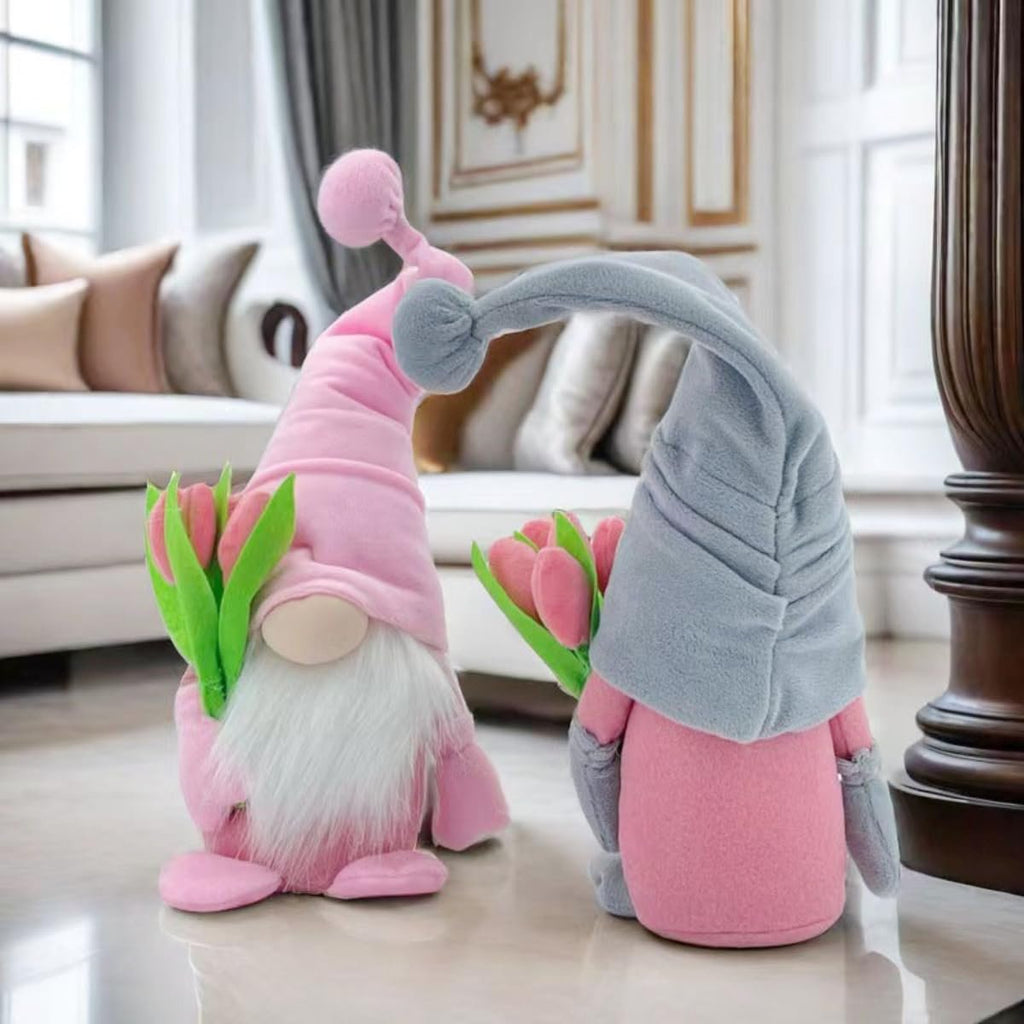 Two plush gnome dolls holding pink tulips, one in a pink hat and one in a grey hat, displayed indoors.