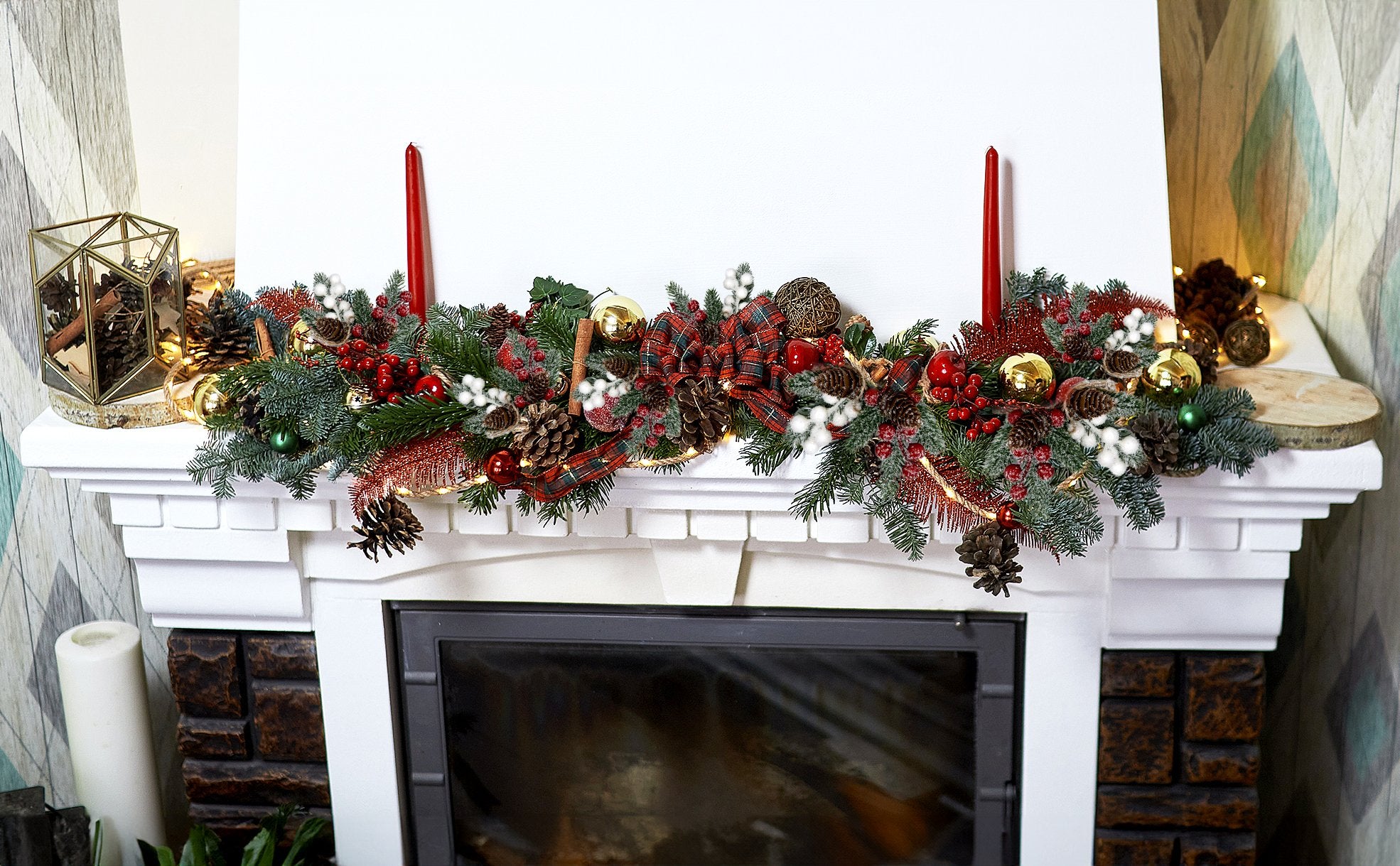Christmas garland with pine branches, red berries, pinecones, gold ornaments, and plaid bows draped over a white mantelpiece.
