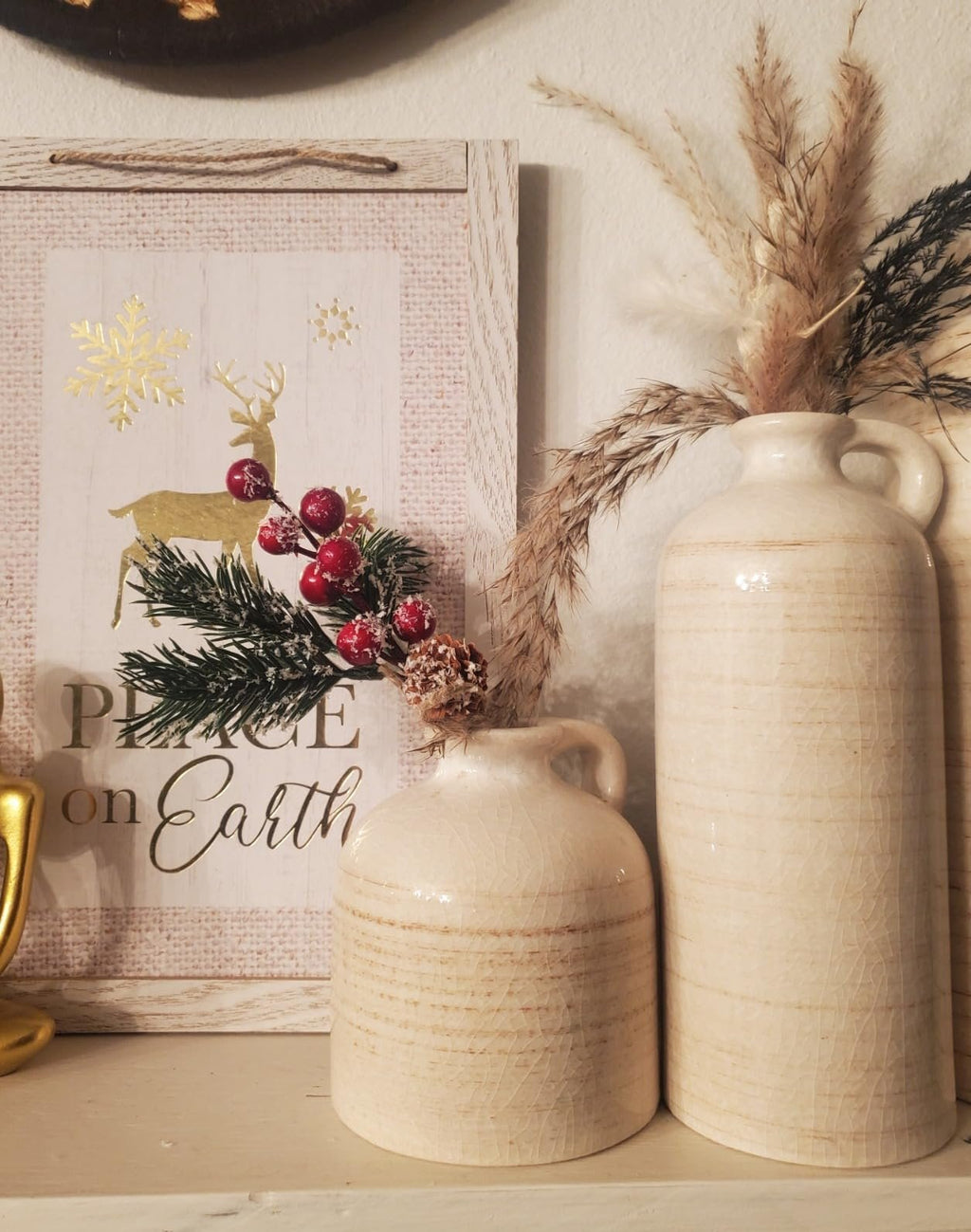 Christmas decorative sign with a deer and snowflake, next to two ceramic vases with dried flowers.