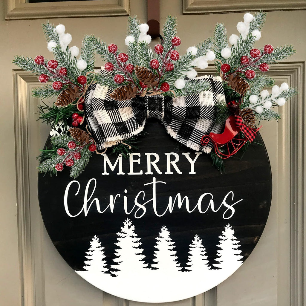 Round wooden Christmas door hanger with 'Merry Christmas' text and frosted pine branches, berries, pinecones, and a buffalo plaid bow.