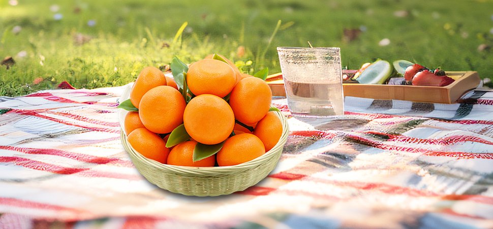 Basket of artificial oranges with green leaves on a picnic blanket with a drink and fruit tray in the background.