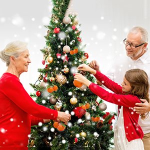 Grandparents and granddaughter decorating a Christmas tree with ornaments and artificial oranges