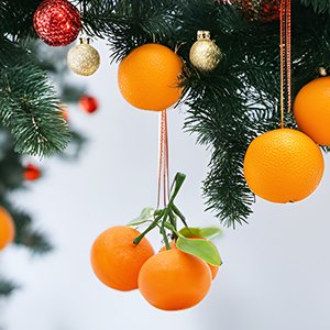 Artificial oranges with green leaves hanging from a decorated Christmas tree with ornaments