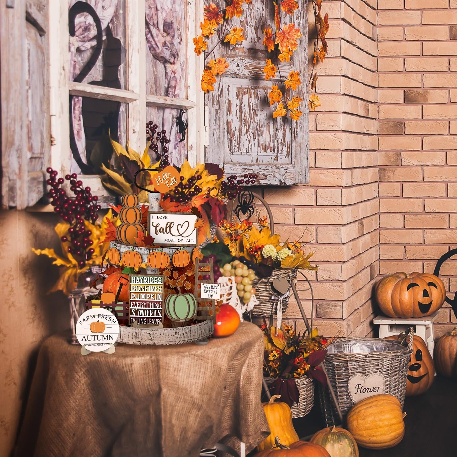 Thanksgiving tiered tray decor set with wood signs, pumpkins, and fall leaves arranged on a table with a brick wall background.