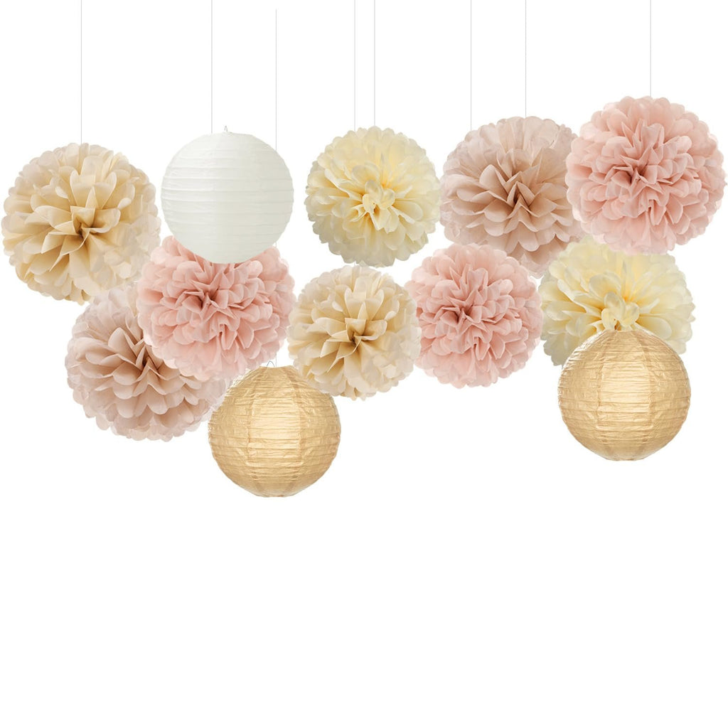 Assortment of hanging paper pom poms and lanterns in cream, pink, and gold colors against a white background.