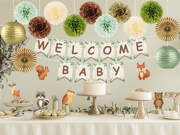 Woodland baby shower decorations with banner, pom poms, paper lanterns, and animal cutouts on a table with cakes and treats.
