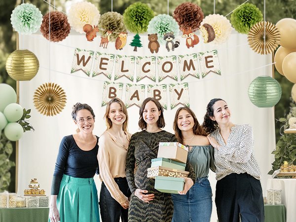Five women smiling at a baby shower with woodland-themed decorations and gifts