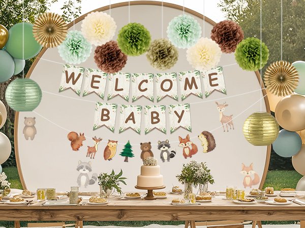 Woodland baby shower decorations including a 'Welcome Baby' banner, pom poms, paper lanterns, and animal cutouts, set up over a table with a cake.